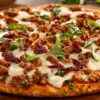 Thin-crust pizza topped with melted mozzarella cheese, seasoned ground chicken, sun-dried tomatoes, and fresh basil leaves